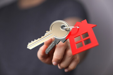 Close-up of a hand holding a house key with a red house-shaped keychain. Symbolizing home...