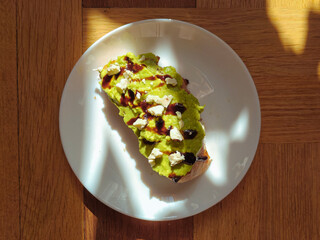 Smashed avocado with spice on the sourdough toast with teriyaki sauce. Protein-packed vegetarian food concept. Wooden background with sunlight. Guacamole.