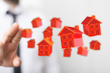 Hand holding or controlling miniature red houses, symbolizing real estate, property investment, and housing market. The image depicts concepts o