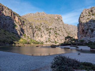 Sa Calobra beach Mallorca, serene canyon with a calm lake surrounded by rugged cliffs, featuring sparse greenery and a solitary tree, Majorca