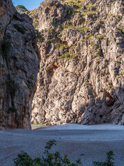 Sa Calobra beach Mallorca, rugged cliff with sparse vegetation frames a serene beach at its base, bathed in sunlight, Majorca