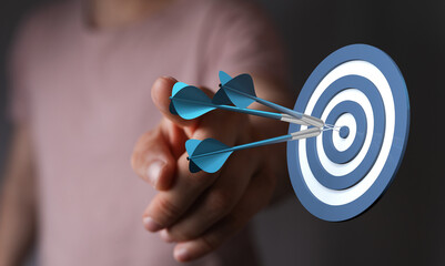 Close-up of a hand throwing darts at a dartboard achieving target. Symbolizing focus, precision,...