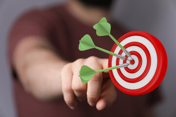 Image of hand pointing at a target, with darts successfully hitting the center. Represents goals,...