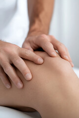 Fototapeta premium Close-up of hands working on a knee. Physiotherapist giving manual therapy to patient with knee joint pain, showing manual techniques to support recovery. Professional and therapeutic touch.