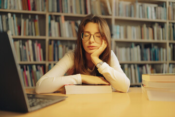 Close portrait of a sleepy student with eyes closed, leaning on a textbook at the library table. Fits messages about rest, balance, time management, and realistic study routines.