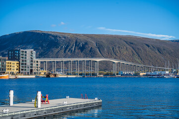 Tromso scenic harbor with Tromsobrua Bridge spanning across the water, surrounded by buildings and a mountain in the background, Norway