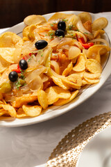 The "Bacalhau com Cebolada", a traditional Portuguese dish made with fried codfish topped with sautéed onions, peppers, and olives, served with crispy round potato chips.