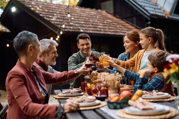 Happy multi-generation family celebrating Thanksgiving and toasting during meal on patio.