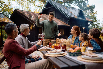 Happy man raising toast while celebrating Thanksgiving with his extended family.
