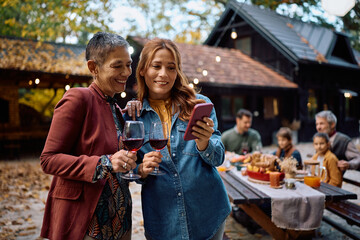 Happy women using cell phone during family Thanksgiving celebration.