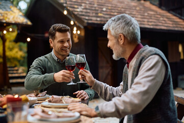 Happy man and his mature father toasting with wine while celebrating Thanksgiving.
