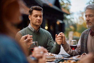 Grateful man and his family holding hands while praying at dining table on Thanksgiving.