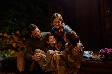 Obraz premium Happy parents talking to their kids while spending evening together in backyard in autumn.