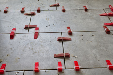 Ceramic floor tile installation with red wedges and white spacers during renovation, close up of...