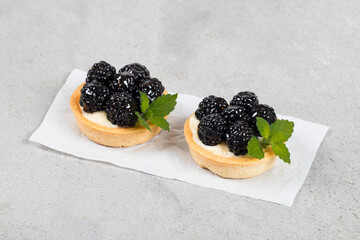 Mini blackberry tart. With custard. Decorated with mint. Light gray background. Close up