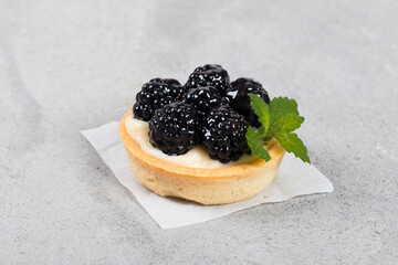 Mini blackberry tart. With custard.Decorated with mint. Light gray background. 