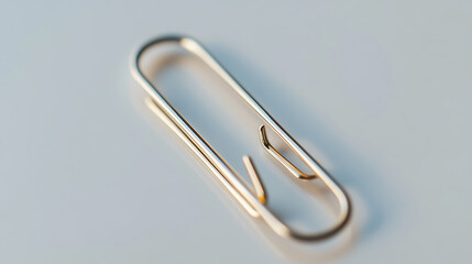 This is a very close up shot of a metal paper clip. The color of the paper clip looks gold in color. The background is white, which gives this shot a clean, neat appearance.