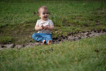 joyful toddler sits on lush grass with a playful smile, hands clasped, surrounded by earthy landscape of pinecones and greenery on a sunny day, environment, tranquil, carefree, wholesome, freedom