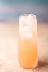 chilled peach-colored beverage with ice cubes in a tall glass set against a softly blurred blue and beige gradient backdrop, evoking a refreshing summery atmosphere and aesthetic, clear, modern