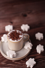 creamy hot chocolate topped with chocolate sprinkles in ribbed ceramic cup on plate, surrounded by white star-shaped marshmallows on rustic wooden table for cozy winter ambiance, elegant, tasty