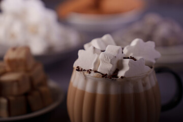 a steaming glass mug filled with creamy hot chocolate topped with star-shaped marshmallows and chocolate sprinkles, surrounded by blurred festive bowls in a cozy, warm setting, cream, fresh
