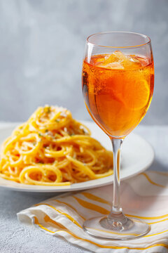 perol spritz cocktail with ice and orange slice beside pasta plate