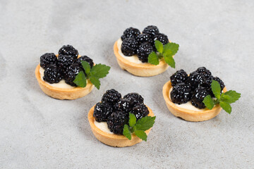 Mini Vegan blackberry tart. Decorated with mint. Light gray background. Close up
