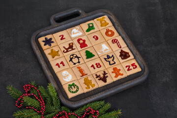 Advent Calendar. 25 festive square cookies with colored curly marmalade filling. On a wooden plate. Dark background. Close up
