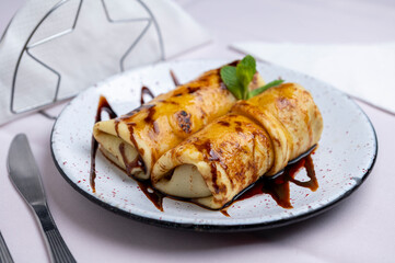 Sweet dessert: homemade egg and milk crepe with caramel, dulce de leche, cream, chocolate, and mint leaves on a china plate.