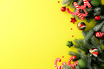 Festive Christmas border with pine branch, candy cane, bauble and star on yellow background,...