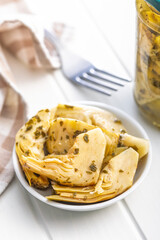 Pickled artichoke in bowl on white table.