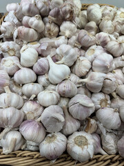 Heap of fresh garlic bulbs nestled in a rustic woven basket, showcasing papery white skins with subtle purple hues and earthy textures for farm-fresh appeal.