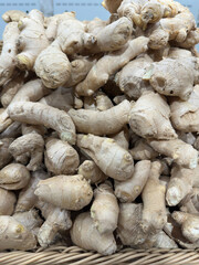Abundant pile of fresh ginger roots with knobby, beige textures and pale skins, arranged in a rustic woven basket for a vibrant market display