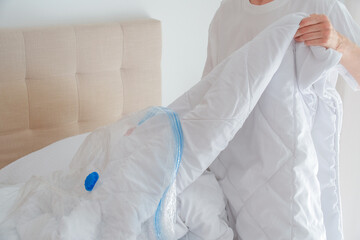 Woman hands putting duvets and pillows into a plastic vacuum sealed bag. Seasonal bedding storage, smart home organization