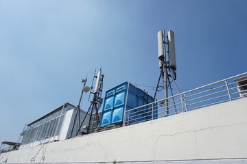 antennas and signal transmitting devices on the roof of a white building with a blue water tank next to it, the clear sky in the background emphasizes the elements of modern technology
