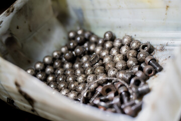 Box of used metal ball bearings and bolts covered in grease and dust showing industrial wear,...