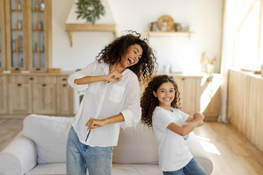 Joyful young mother and preteen daughter dancing together in living room at home, mom having fun with girl child, enjoy spending time together