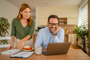 Couple working from home using laptop during breakfast