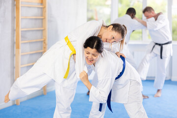 Skillful middle-aged female judo practitioners engaged in wrestling during workout session