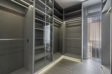 A spacious walk-in closet showcases gray shelving and glass doors, with soft lighting highlighting the organized storage. Natural light flows in through a nearby window.