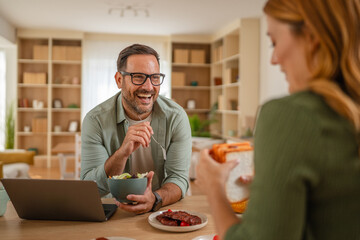 Happy couple enjoying breakfast laughing together at home