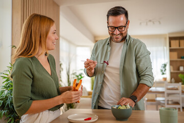 Smiling couple preparing healthy salad in modern kitchen