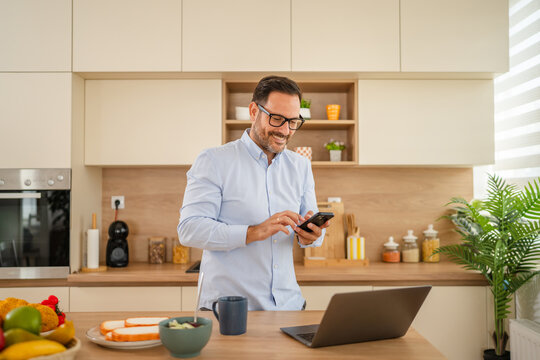 Happy man using smart phone during remote work breakfast - Powered by Adobe