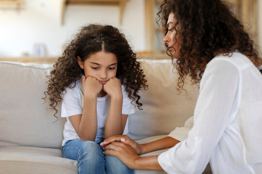Family support and mother care. Caring loving mother calming sad preteen daughter, talking about girl problems, sitting on sofa at home