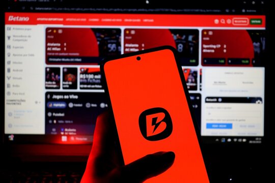 Betano logo on smartphone screen and Betano website on laptop. Online sports betting platform.