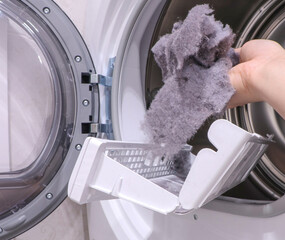 close up female hand taking lint out from dirty air filter of dryer machine after drying. cleaning...