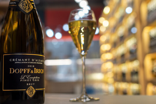 Bottle of Dopff and Irion Cr&eacute;mant d'Alsace L'Exception Pinot Gris Brut against background with flute glass in warmly lit wine shop setting with blurred shelves. Ukraine, Zhytomyr, October, 28, 2025