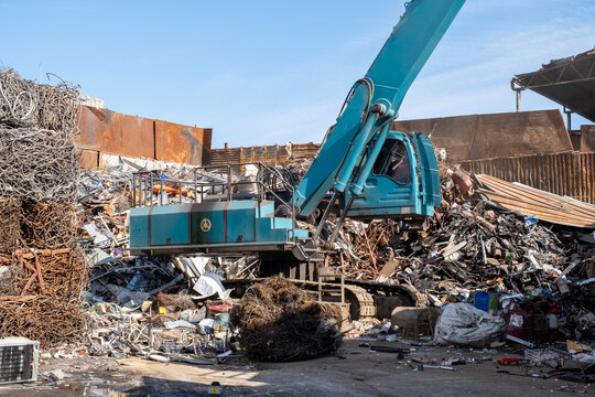 Excavator loading scrap metal onto truck in junkyard. Industrial excavator working at metal recycling yard. Excavator handling metal waste at recycling facility. - Powered by Adobe