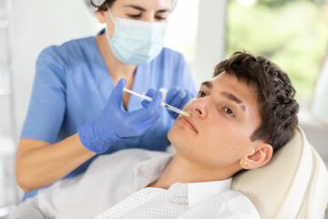 Fototapeta premium Young male patient lying on clinical chair undergoing face care procedure by injection method