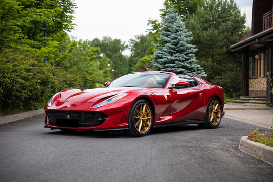 Ferrari 812 GTS: Striking red convertible supercar on a scenic drive through a green forest landscape logo detail 
